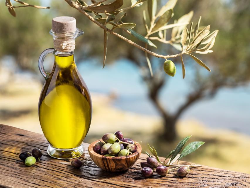 Olive oil and berries are on the wooden table under the olive tree.