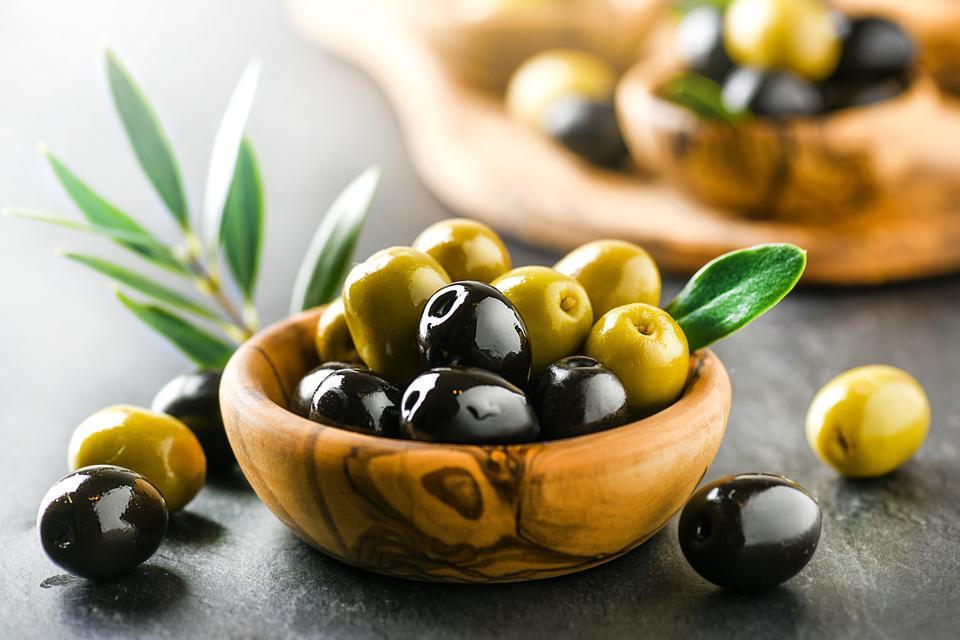 Fresh olives with core in olive bowl on dark stone table and green leaves.